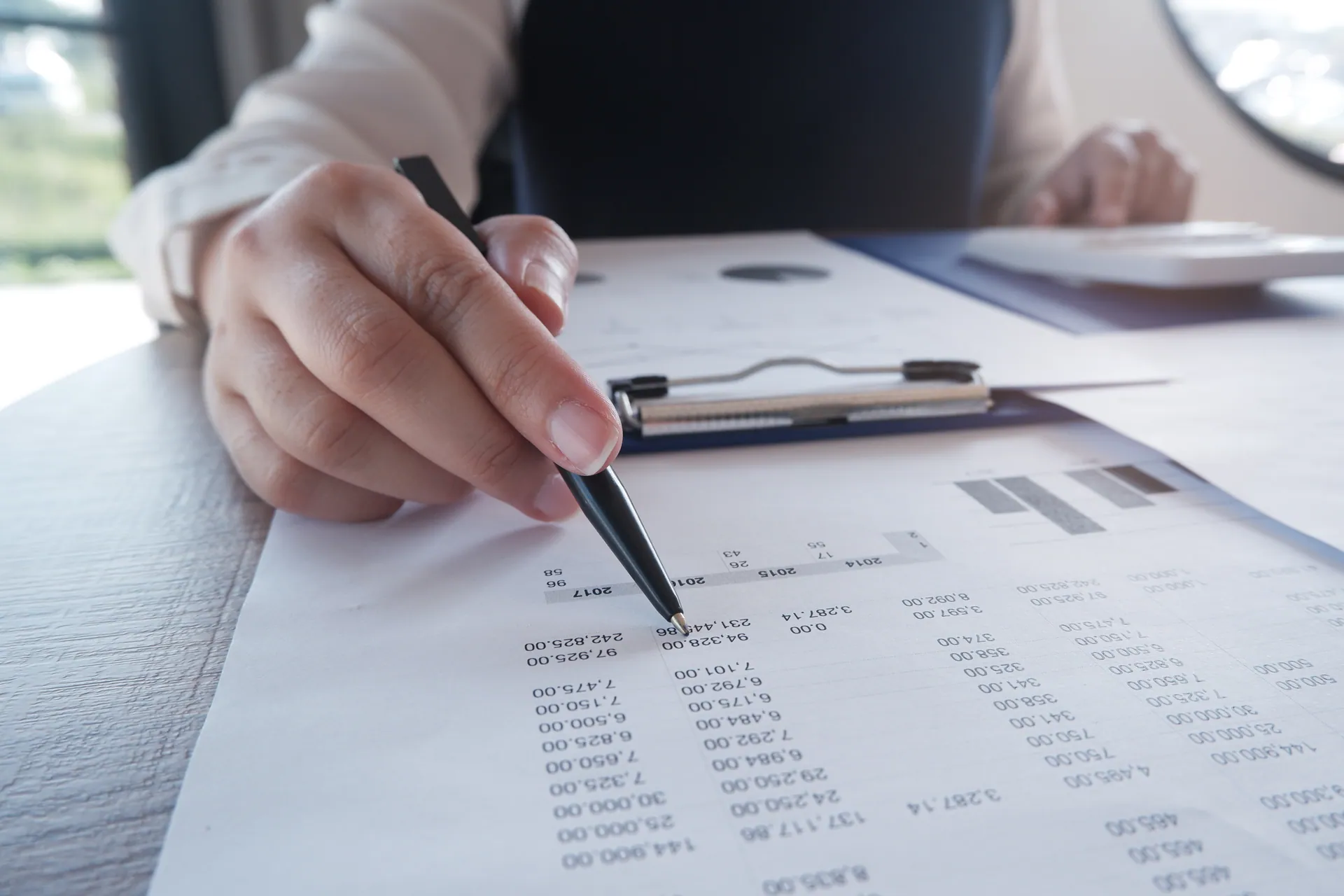Person reviewing a financial statement with a pen next to a clipboard and calculator